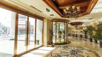 A hotel lobby with a glass entrance, a chandelier, and a patterned floor.