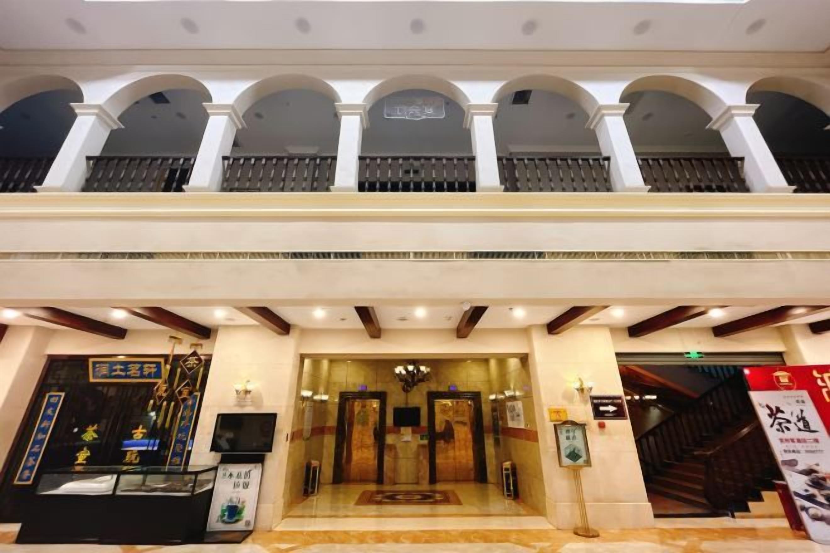A hotel entrance with a reception desk, a staircase, and a balcony with columns.