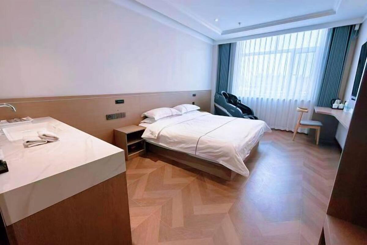 Habitación de hotel con cama, mesita de noche, silla, escritorio y ventana con cortinas.