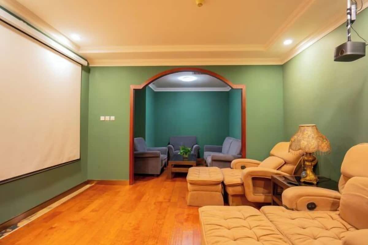 Una sala de estar con una pared verde, piso de madera, una pantalla de proyector, un sofá, un sillón y una lámpara.