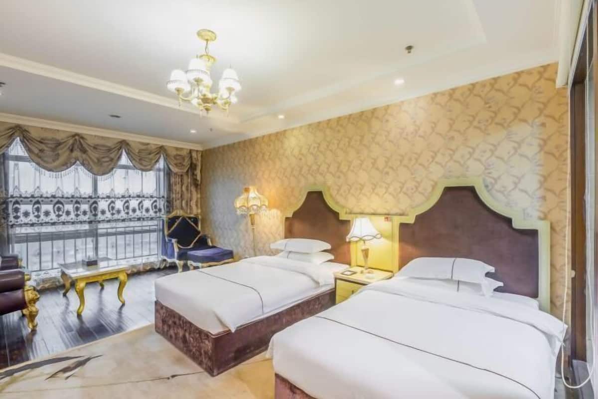 Habitación de hotel con dos camas, una araña, papel tapiz estampado y vistas a través de una ventana con cortinas.