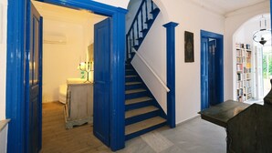 Een trap met blauwe leuningen en witte treden, die uitkomt op een plateau met een boekenplank en een lamp.