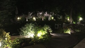 Een tuin met verlichte planten en bomen, een pad en buitenmeubilair.