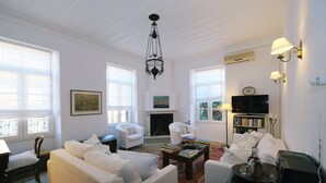 Een ruime woonkamer met witte meubels, een open haard, een televisie en een boekenkast.
