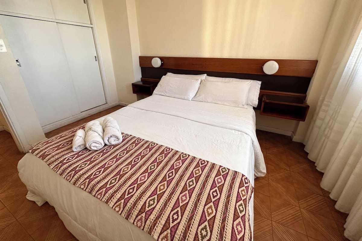 A neatly made bed with a patterned bedspread, a wooden headboard, and a nightstand with a lamp.
