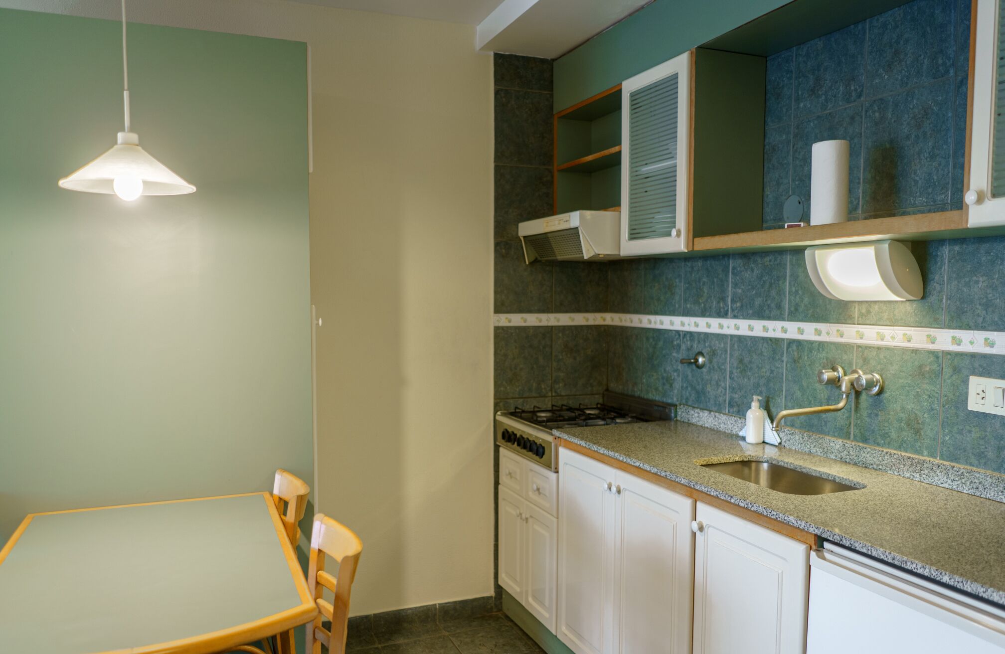 A kitchen with a dining table and chairs, a gas stove, a sink, and a hanging light fixture.