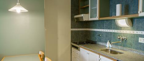 A kitchen with a dining table and chairs, a gas stove, a sink, and a hanging light fixture.