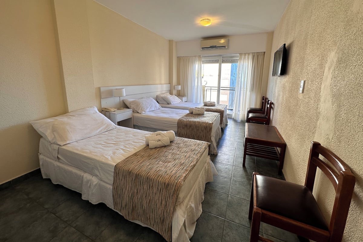 A hotel room with three beds, a TV mounted on the wall, and a small table with chairs.