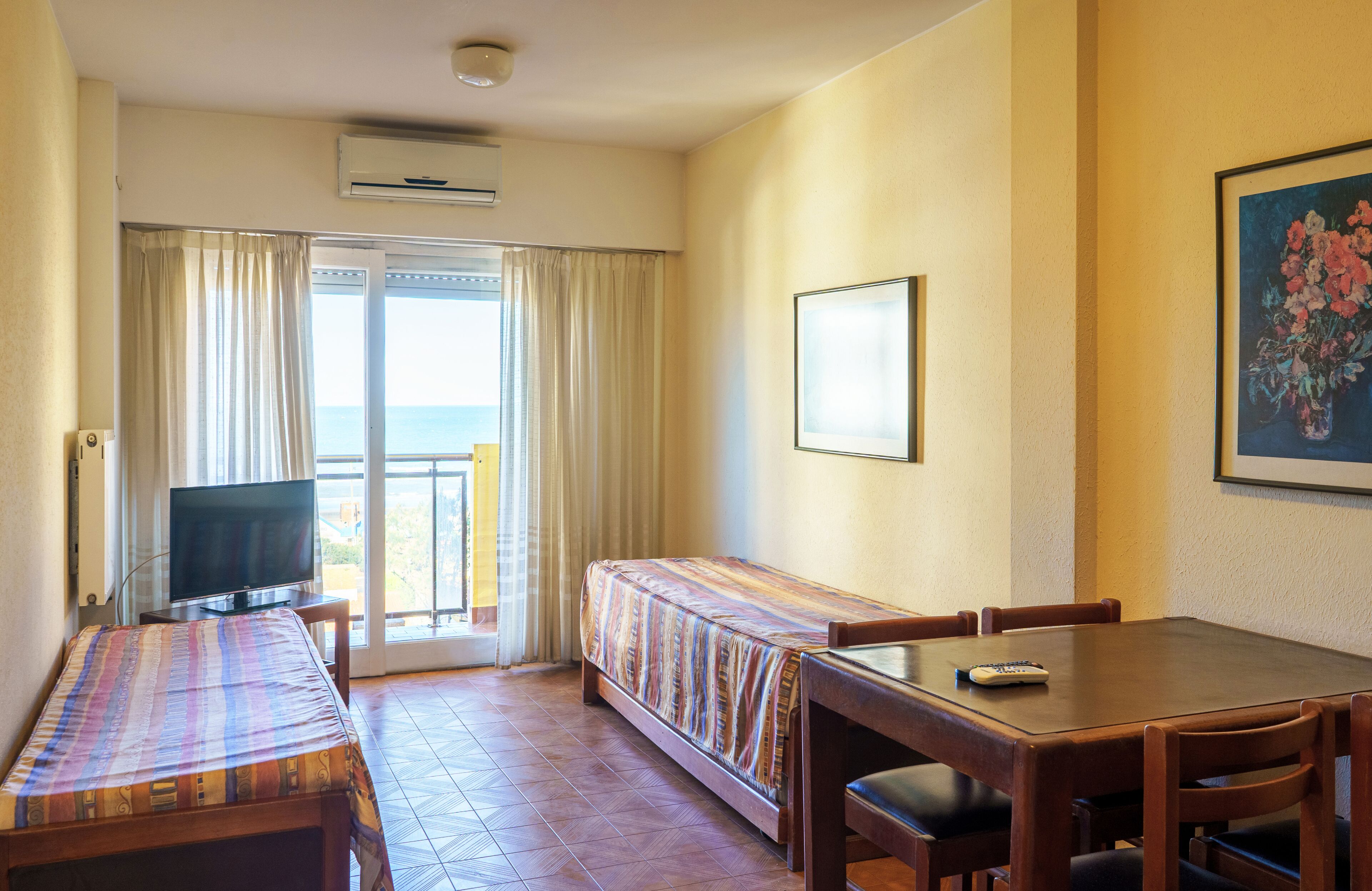 Habitación de hotel con cama, televisor, mesa de comedor y balcón con cortinas.
