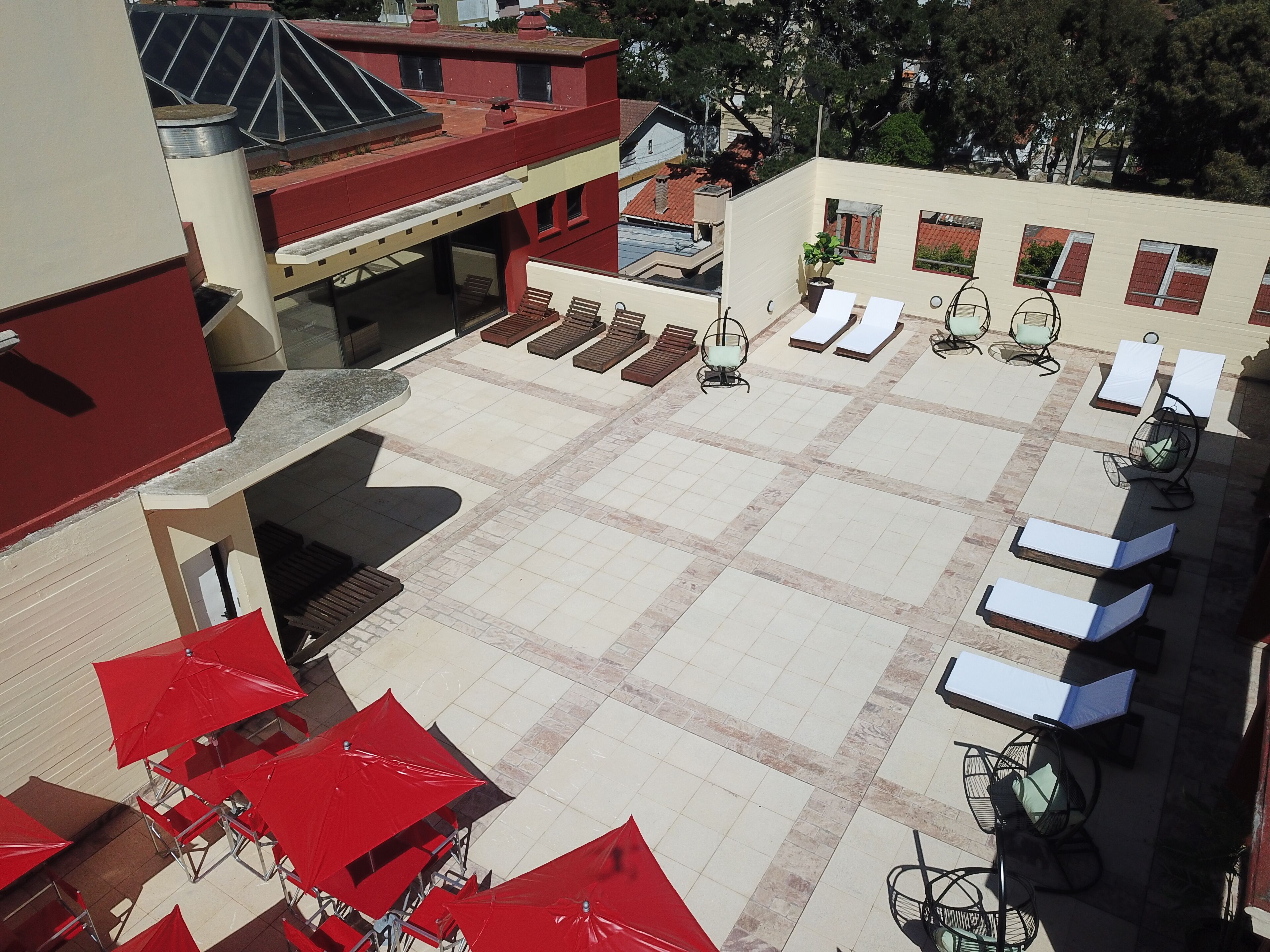 Terraza en la azotea con sillones de sol y sombrillas rojas, un área de estar cubierta y vistas de edificios circundantes.