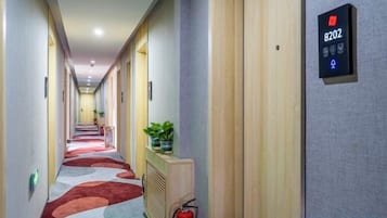 Un pasillo de hotel con un extintor, una planta en maceta y un panel de control de ascensor digital.