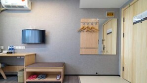 Habitación de hotel con cama, escritorio, televisor, armario y zapatero.