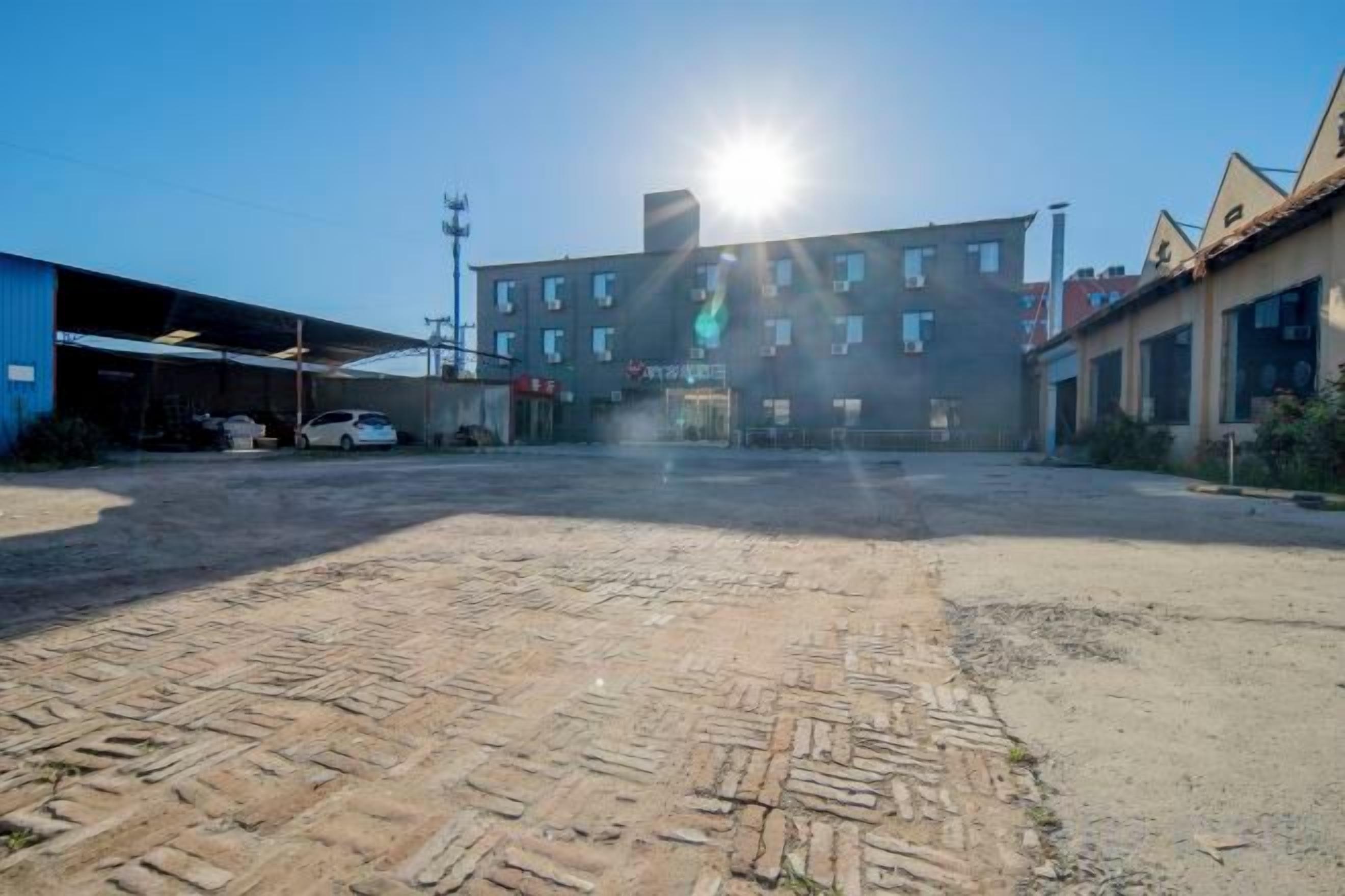 An industrial area with a large building, a dirt ground, and a clear sky.