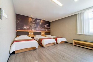 A hotel room with three beds, a bench, a cityscape mural, and a wooden floor.