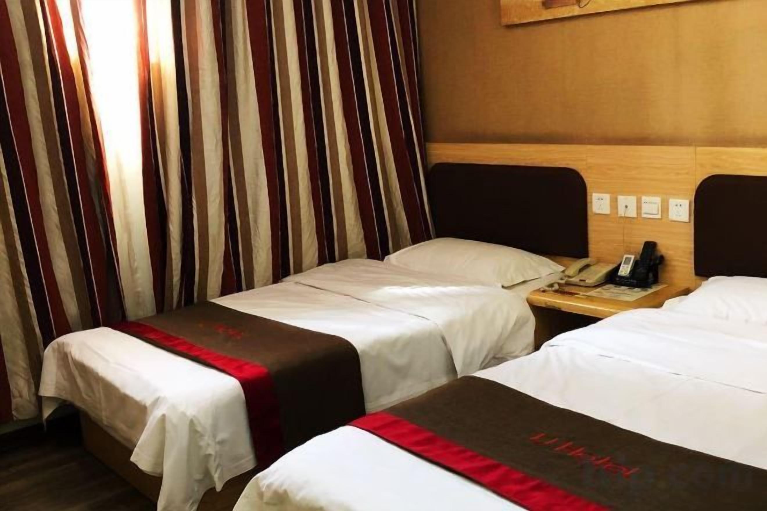 A hotel room with two beds, a wooden headboard, a nightstand with a telephone, and a window with curtains.