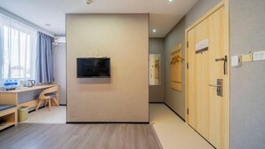 Habitación de hotel con un escritorio de madera, un televisor de pantalla plana montado en la pared y una puerta de madera con manija.