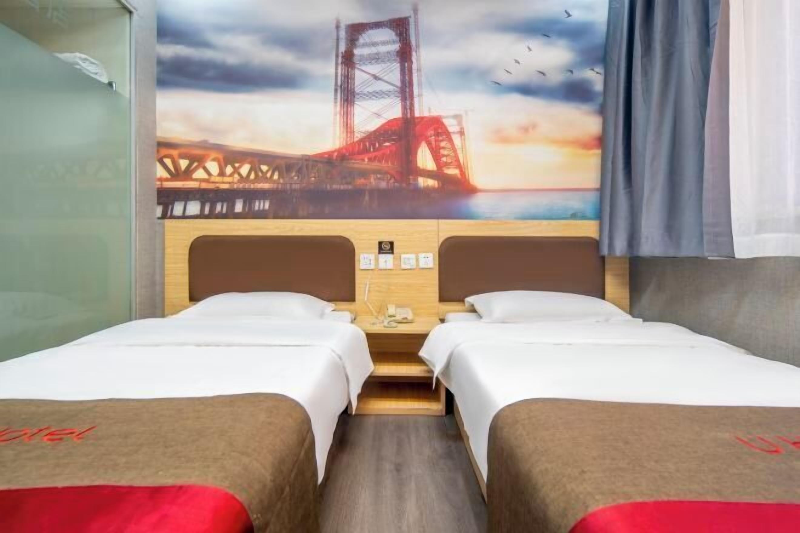 A hotel room with two beds, a wooden headboard, a nightstand, and a large window with a view of a bridge.