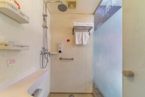 A bathroom with a shower, a toilet, and a sink. There are towels hanging on a rack and a soap dispenser on the wall.