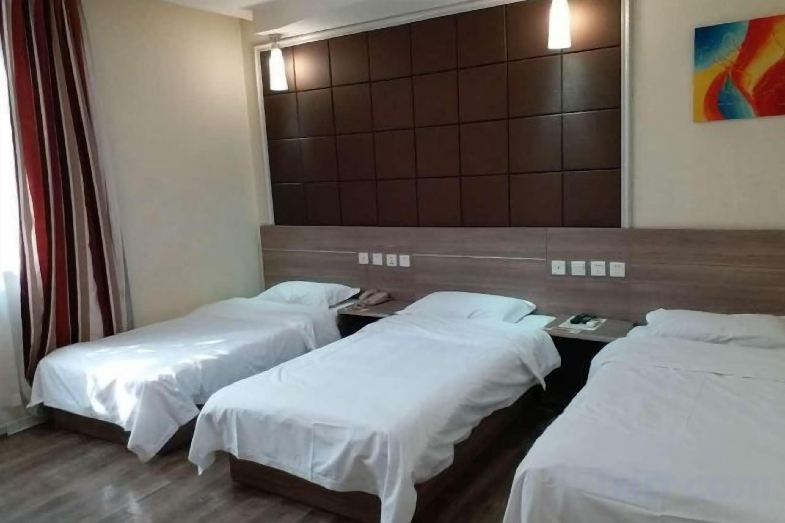 A hotel room with three single beds, a large padded headboard, and a colorful abstract painting on the wall.