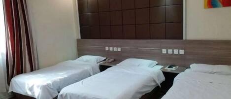 A hotel room with three single beds, a large padded headboard, and a colorful abstract painting on the wall.