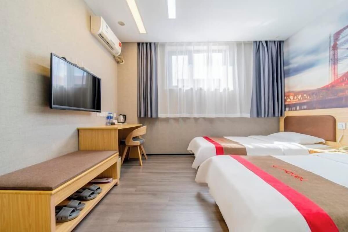 A hotel room with a bed, a desk, a TV, and a window with curtains.