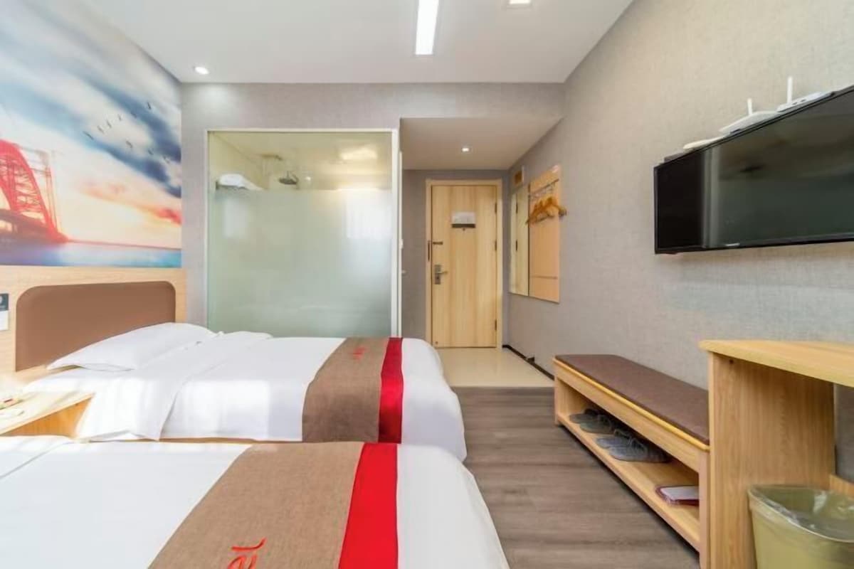 A hotel room with two beds, a TV, a desk, and a bookshelf.