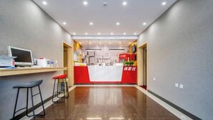 Vestíbulo de hotel con mostrador de recepción, dos taburetes de bar, televisor de pantalla plana y suelo limpio y pulido.