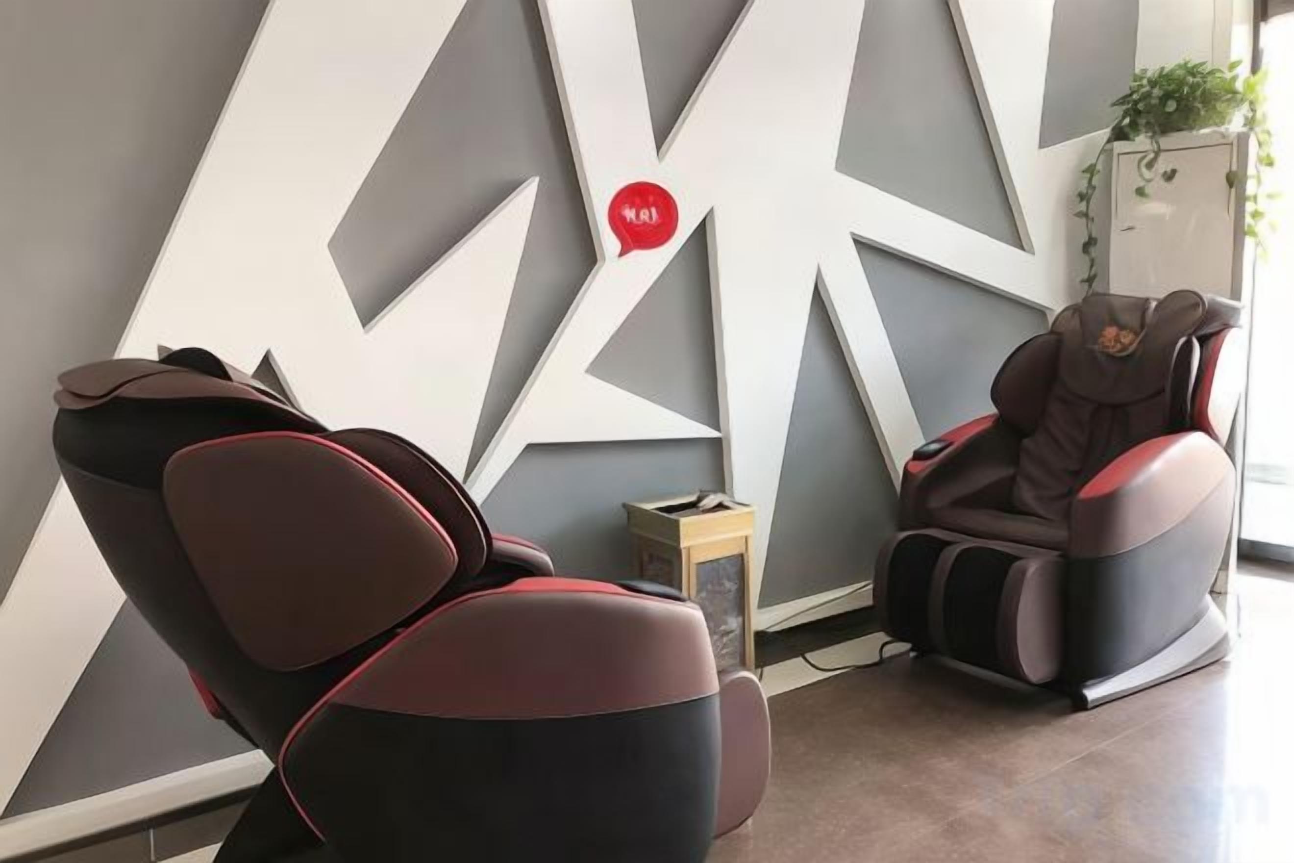 Un fauteuil de massage et une table de massage dans une pièce dont le mur est orné d’un motif géométrique, avec une petite table sur laquelle est posée une plante.