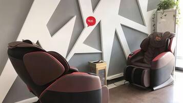Un fauteuil de massage et une table de massage dans une pièce dont le mur est orné d’un motif géométrique, avec une petite table sur laquelle est posée une plante.