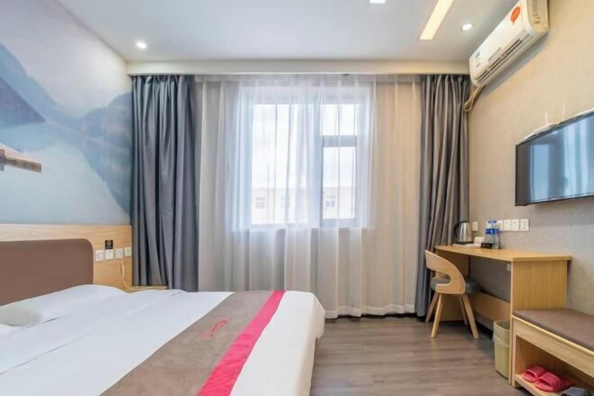 A hotel room with a bed, a desk, a chair, a TV, and a window with curtains.