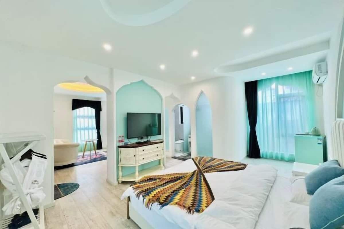 A hotel room with a bed, a TV, a dresser, and a bathroom visible through an archway.