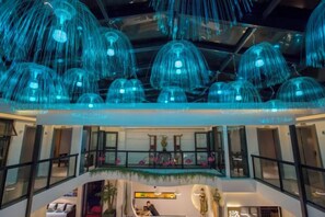 Un atrio de varios niveles con lámparas azules colgantes, barandillas de cristal y plantas de interior.