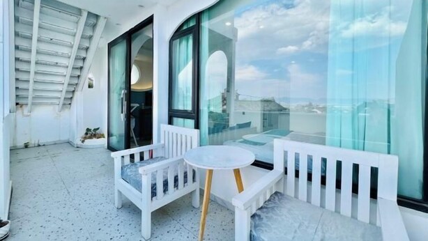 A balcony with white furniture, including a bench and a small table, and large windows offering a view of the city. - Hotel Du Temps Perdu (Dali City)