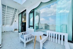 Un balcon doté de mobilier blanc, comprenant un banc et une petite table, et de grandes fenêtres offrant une vue sur la ville.
