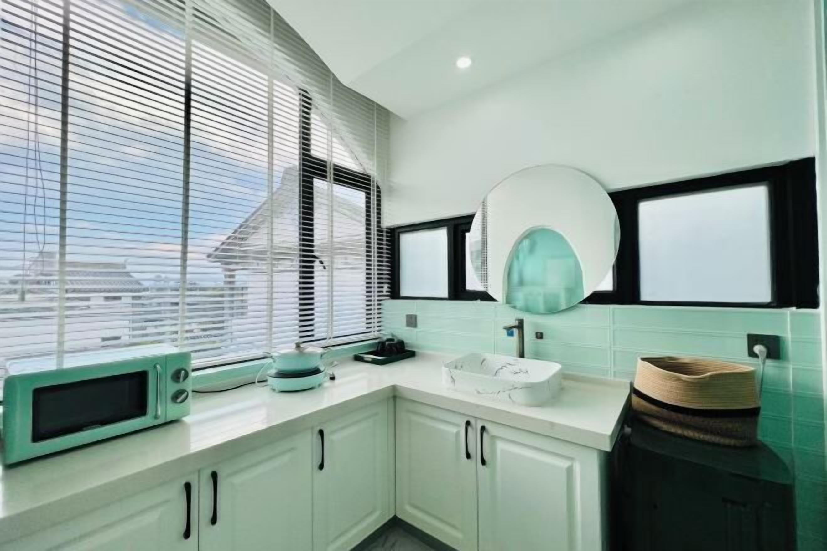 A modern kitchen with white cabinets, a teal-colored microwave, and a large window with blinds.