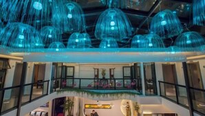 A multi-level hotel lobby with a modern design, featuring a central staircase, seating areas, and decorative elements like flamingos and a statue. - Hotel Du Temps Perdu (Dali City)