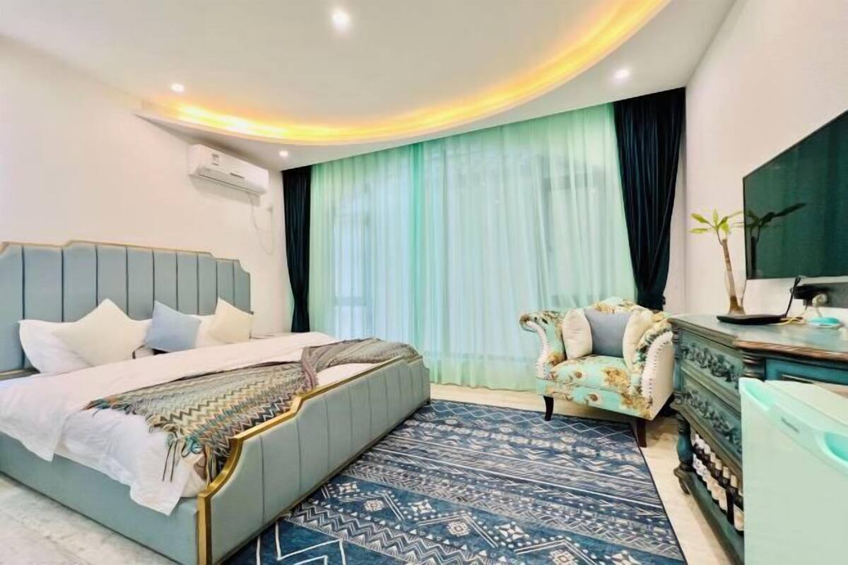 A bedroom with a bed, a vanity, and a large window with sheer curtains.