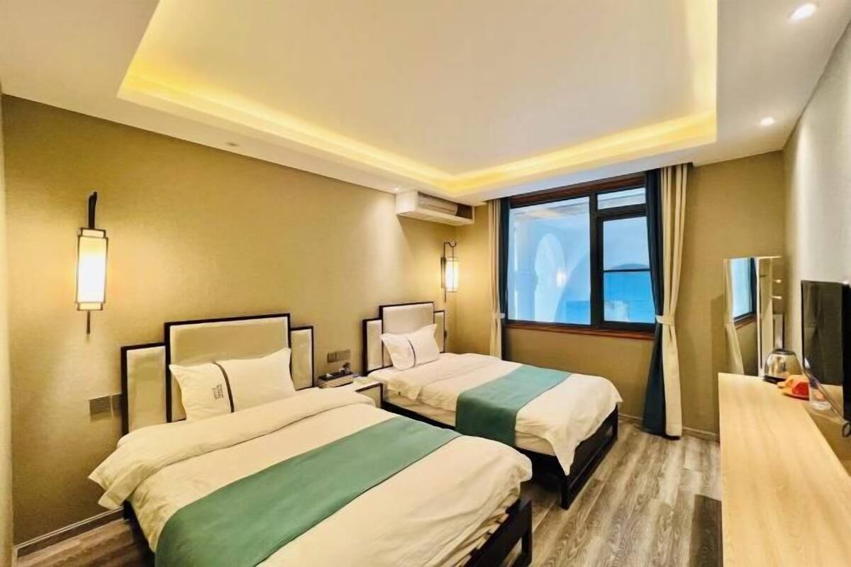 A hotel room with two beds, a desk, a TV, and a window with a view.
