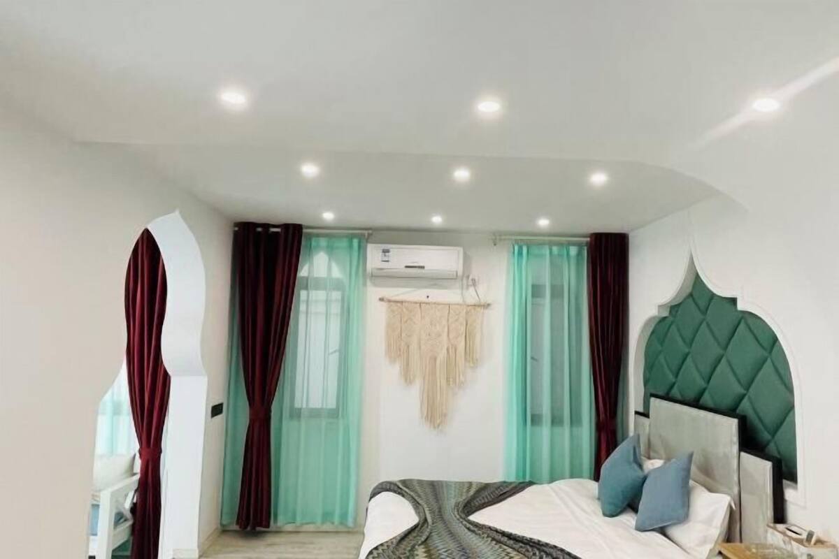 A modern bedroom with a bed, curtains, an air conditioning unit, and a unique green headboard.