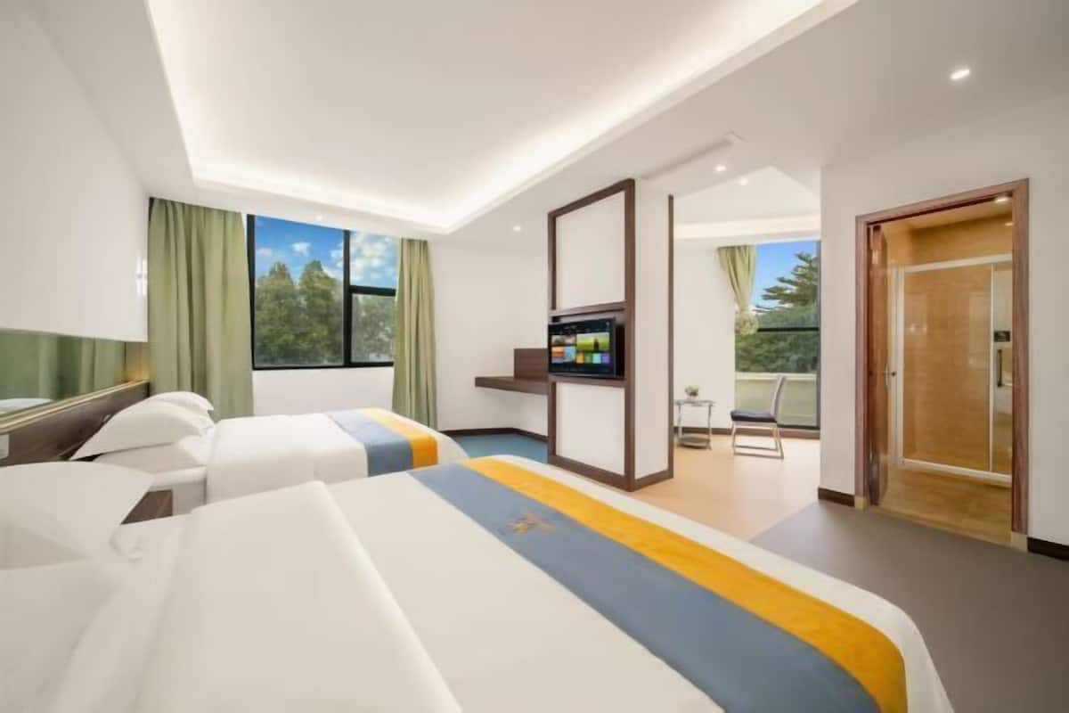 A hotel room with two beds, a TV, a balcony, and a view of trees.