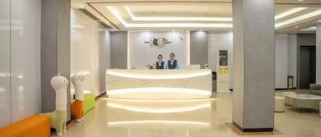 A hotel reception area with a curved reception desk, a seating area with a bench, and a large pillar.