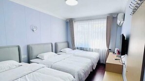 Ein Hotelzimmer mit drei Betten, einem Schreibtisch und einem Fernseher.