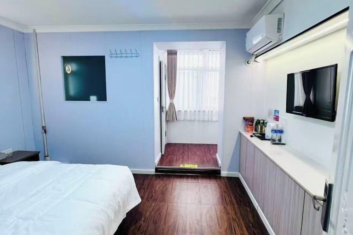 A hotel room with a bed, a television, a small window with curtains, and a radiator.