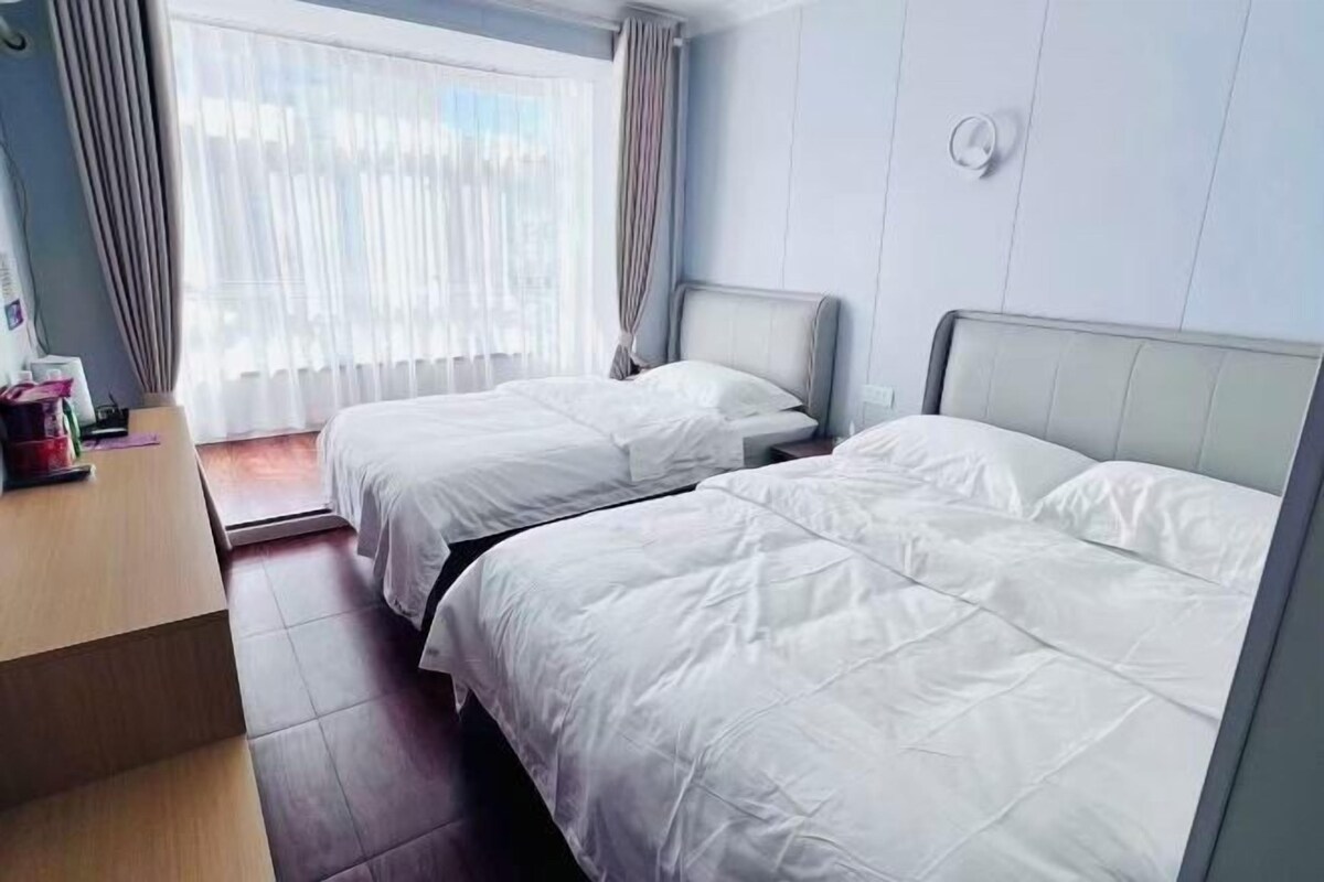 A hotel room with two beds, a wooden desk, and a window with curtains.