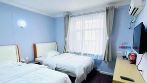 Ein Hotelzimmer mit zwei Betten, einem Schreibtisch, einem Fernseher und einem fenster mit Vorhängen.