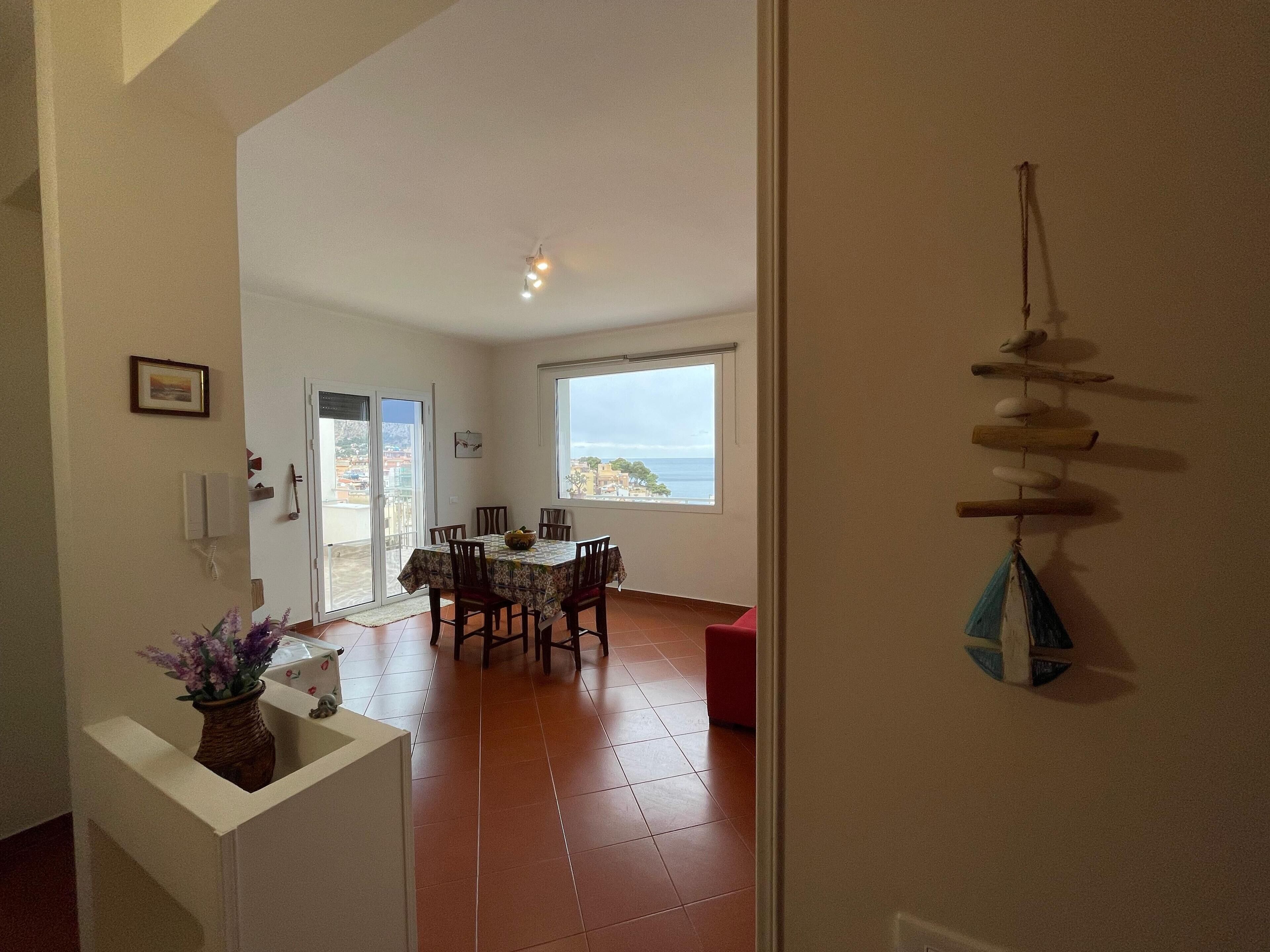 Un coin repas avec une table et des chaises, une vue sur la mer par une fenêtre et une décoration murale.