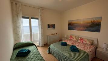 Ein Schlafzimmer mit zwei Betten, einem großen Fenster mit Vorhängen, einem Gemälde an der Wand und einer Deckenleuchte.