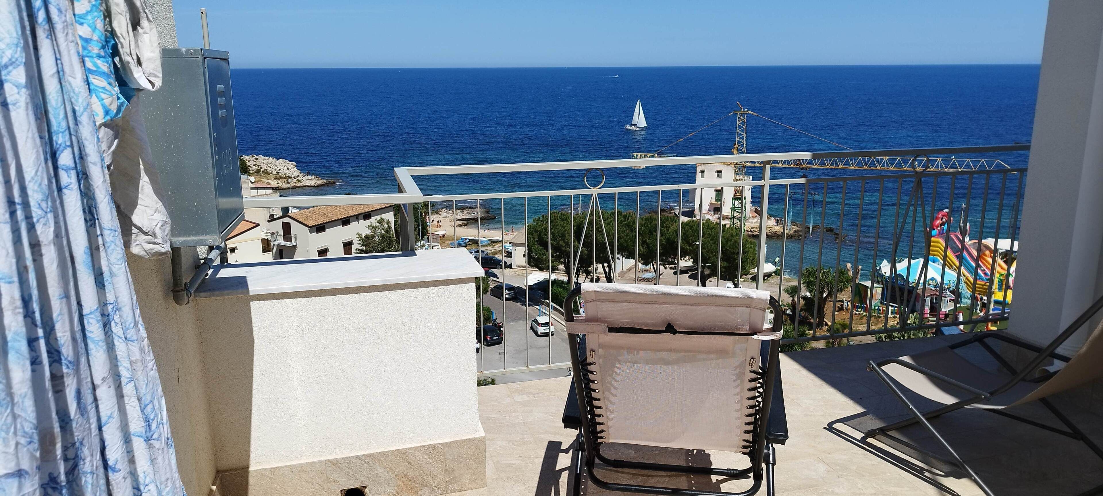 Un balcon avec vue sur la mer, un voilier et une aire de jeux colorée.