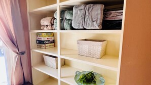 A room with a white shelving unit containing various items including boxes, a woven basket, and a decorative plate. - Home Away from Home- Discover Comfort and Convenience in this 4 Bedroom Home  (Holden)