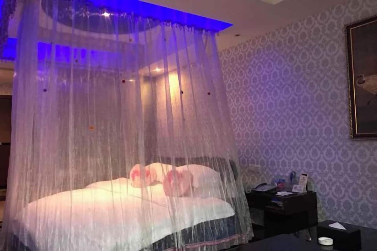 A room with a bed under a canopy, a nightstand, and a wall with patterned wallpaper.